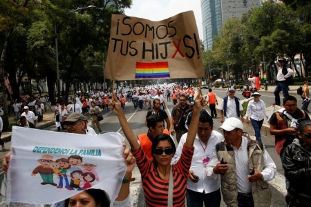 A woman holds a sign near the Angel of Independence monument in support for the legalization of gay marriage while others behind participate in a protest march against it and defend their interpretation of traditional family values, in Mexico City, Mexico September 24, 2016. The sign reads: "We are your Children."