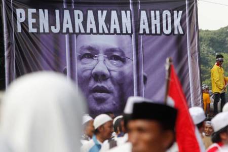 Members of hardline Muslim groups stand around a poster during protest against Jakarta's incumbent governor Basuki Tjahaja Purnama. The poster reads