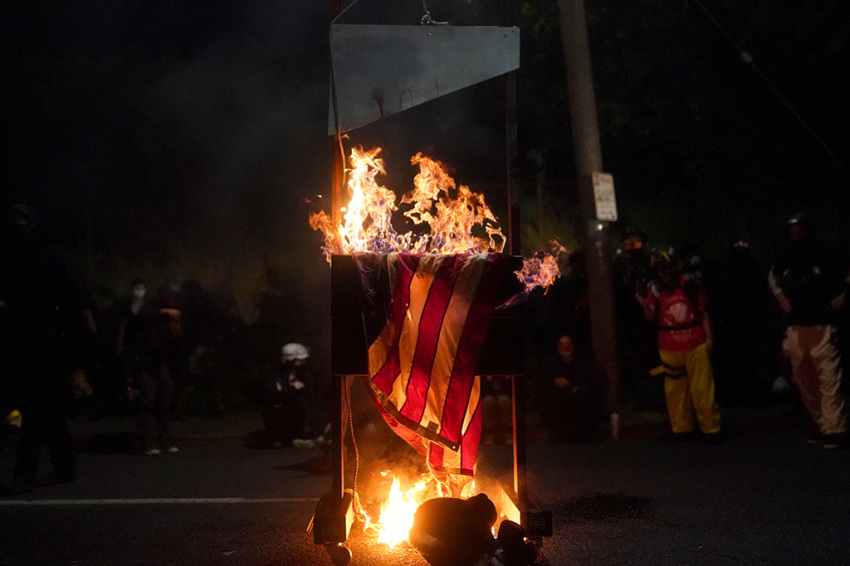 An American flag burns on a guillotine in front of the Multnomah County Sheriffs Office on August 22, 2020, in Portland, Oregon. Hundreds of rioters clashed with police Saturday night following a rally in east Portland.