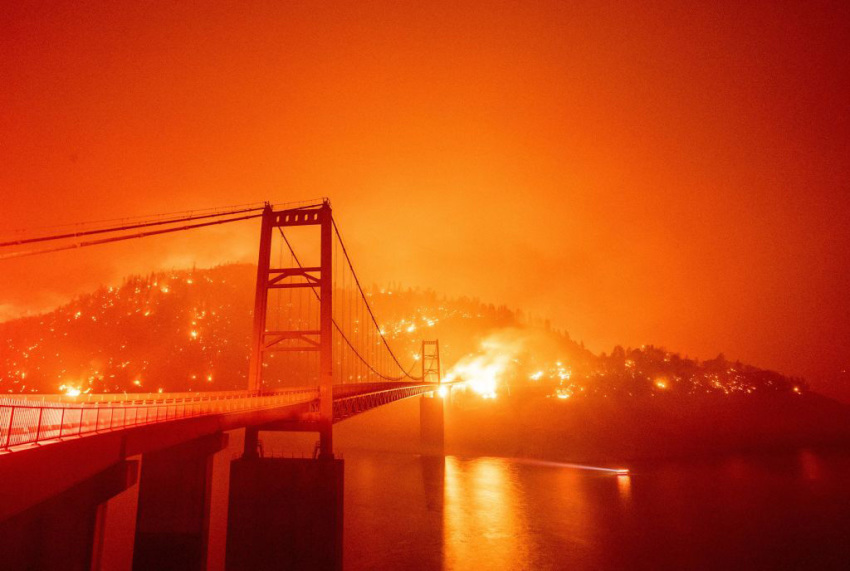 A boat motors by as the Bidwell Bar Bridge is surrounded by fire in Lake Oroville during the Bear fire in Oroville, California on September 9, 2020. - Dangerous dry winds whipped up California's record-breaking wildfires and ignited new blazes Tuesday, as hundreds were evacuated by helicopter and tens of thousands were plunged into darkness by power outages across the western United States.