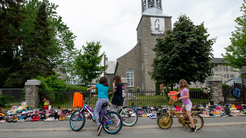 Local children of Kahnawake, Quebec stop on May 30, 2021, to view the hundreds of children's shoes placed in front of the St. Francis Xavier Church, as members of the community of the Kahnawake Mohawk Territory, Quebec, commemorate the news that a mass grave of 215 Indigenous children was found at the Kamloops Residential School in British Columbia, Canada. The remains of 215 Indigenous children have been found buried on school's grounds, which closed in 1978. With the help of a ground-penetrating radar specialist, the stark truth of the preliminary findings came to light -- the confirmation of the remains of 215 children who were students of the Kamloops Indian Residential School,