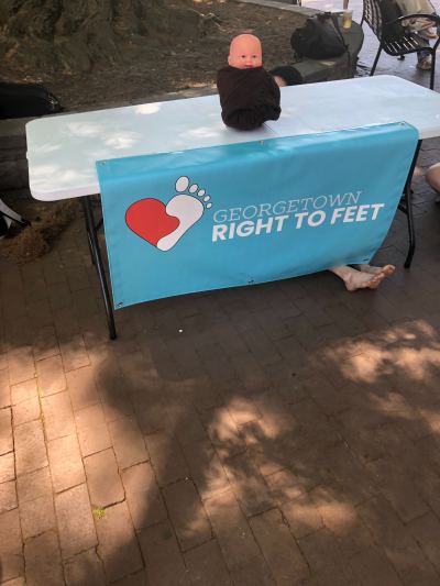 A Georgetown University student sits behind a "Georgetown Right to Feet" banner while Students for Life of America President Kristan Hawkins talks about abortion on campus on Thursday, April 20, 2023.