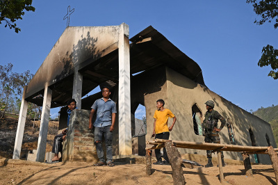 An Indian army soldier (R) stands along with villagers in front of a ransacked church that was set on fire by a mob in the ethnic violence hit area of Heiroklian village in Senapati district, in India's Manipur state on May 8, 2023. Around 23,000 people have fled the unrest which erupted last week in the hilly northeast state bordering Myanmar. The latest clashes erupted between the majority Meitei people, who are mostly Hindu, living in and around the Manipur capital Imphal and the mainly Christian Kuki tribe of the hills.
