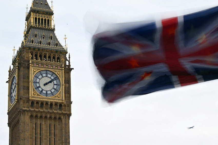 A photograph taken on January 31, 2024, shows a Union Jack flag with behind a a European Union flag flapping in the air in front of the Elizabeth Tower, commonly known by the name of the clock's bell