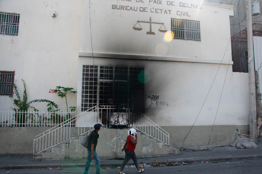 People walk by and look at the tribunal set on fire the previous day by armed gangs, in Port-au-Prince, Haiti, March 6, 2024. Haiti's capital was largely shut down March 4, 2024, with residents only venturing out for essentials, AFP reporters witnessed, as authorities imposed a state of emergency after an attack on a prison freed thousands of inmates.