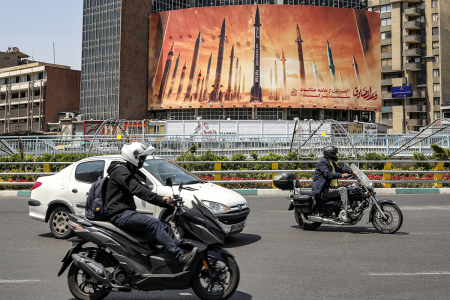 Motorists drive their vehicles past a billboard depicting named Iranian ballistic missiles in service, with text in Arabic reading