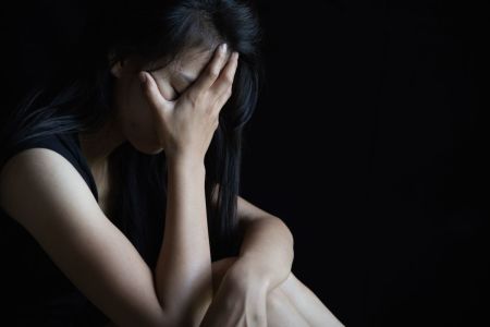 A girl sits alone with a hand over her face.