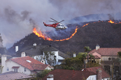 A helicopter flies over homes threatened by the wind-driven Palisades Fire in Pacific Palisades, California, Jan. 7, 2025. A fast-moving brushfire in a Los Angeles suburb burned buildings and sparked evacuations as "life threatening" winds whipped the region. More than 200 acres (80 hectares) was burning in Pacific Palisades, a upscale spot with multi-million dollar homes in the Santa Monica Mountains, shuttering a key highway and blanketing the area with thick smoke.