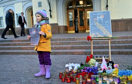 A girl holds a placard as she stands near candles placed as a makeshift memorial outside the National Opera of Ukraine in Kyiv on March 16, 2025, during a commemorative event marking the third anniversary of the Russian bombing of the Mariupol Drama Theatre, amid the Russian invasion of Ukraine. The theatre in Mariupol was used as an air raid shelter during the siege of Mariupol, sheltering a few hundreds of civilians, most of whom died there.