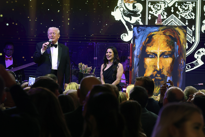President Donald Trump speaks to guests during a New Year’s Eve event at his Mar-a-Lago home on Dec. 31, 2025, in Palm Beach, Florida. "Christian worship painter" Vanessa Horabuena stands next to him in front of her painting of Jesus, which sold for $2.75 million to benefit charity.