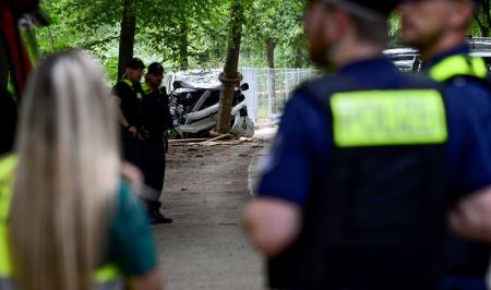 Police work near the wreckage of a car on July 26, 2026, in the Tiergarten park in Berlin, Germany, where a car was driven the evening before into people, killing one person and injuring 16, on the outskirts of the Christopher Street Day (CSD) parade. 