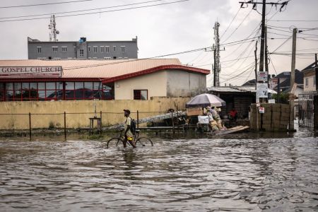 A cyclist pushes his bicycle as he wades through a flooded street in Lekki neighbourhood in Lagos, on July 03, 2026.