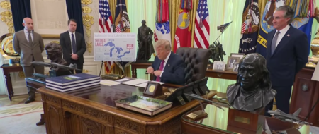 President Donald Trump signs an executive order renaming Lake Ontario as Lake America as a map with the words "Lake America" on it appears behind him, Aug. 27, 2026.