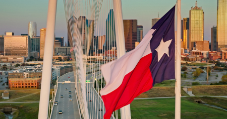 Texas state flag flying over the Margaret Hunt Hill Bridge and the downtown Dallas skyline