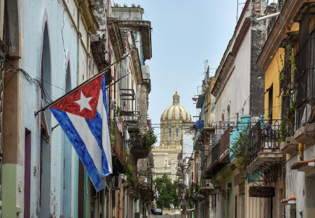 A Havana street with the Cuban flag and Museo de la Revolucion dome in the background.