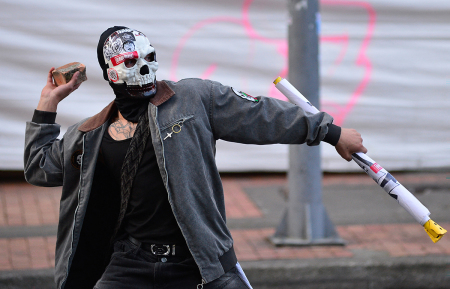A demonstrator throws a stone towards police officers during a protest in front of National Museum against a government order to remove works alluding to LGBT ideology and other works in Bogota on Oct. 18, 2026. Colombia's new government has ordered one of the country's top museums to remove dozens of works alluding to LGBT ideology, sparking condemnation from visitors. 