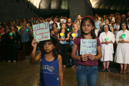 Syrian girls hold up signs as Lebanese and Syrian Christian Maronites pray for peace in Syria, in Harisa, Jounieh September 7, 2013. The signs read, "For Syria we pray" (L) and "Syria, the love and peace" (R).