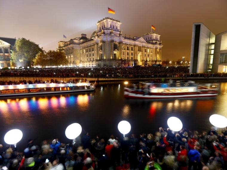 People stand outside the Reichstag lower house of parliament builiding under lit balloons, which are part of the installation "Lichtgrenze" (Border of Light) in Berlin, November 9, 2014. A part of the inner city of Berlin is being temporarily divided from November 7 to 9, with a light installation featuring 8000 luminous white balloons, following the 9.5-mile (15.3 kmilometre) path the Berlin Wall once occupied, to commemorate the 25th anniversary of the fall of the Wall.
