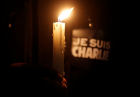 A person holds a candle in front a placard which reads 