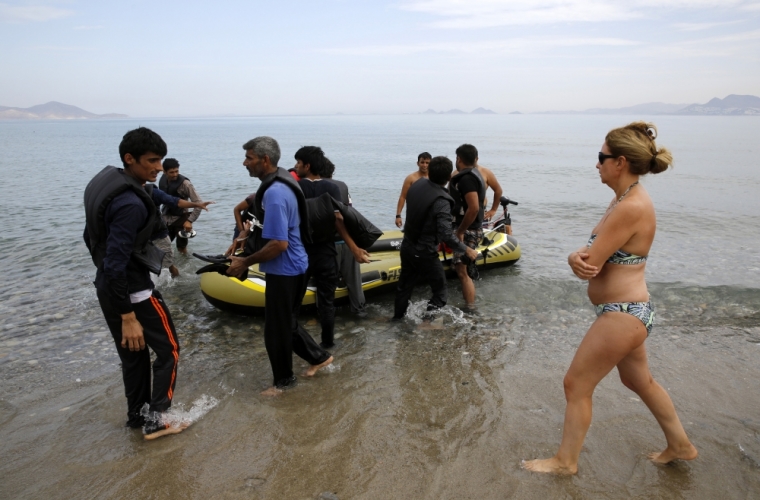 A Spanish tourist watches Pakistani migrants arriving at a beach in the Greek island of Kos after paddling an engineless dinghy from the Turkish coast, August 15, 2015. United Nations refugee agency called on Greece to take control of the "total chaos" on Mediterranean islands, where thousands of migrants have landed. About 124,000 have arrived this year by sea, many via Turkey, according to Vincent Cochetel, UNHCR director for Europe.