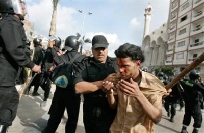 An injured Coptic protester is led away by police, as other policemen fire volleys of tear gas at protesters outside the St. Maximus Church in the northern Mediterranean city of Alexandria, Egypt Sunday, April 16, 2006. Police fired live ammunition into t