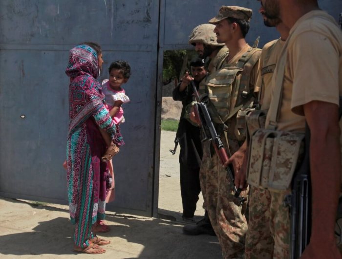 A woman carrying a girl walks past army soldiers who are standing guard at an entrance gate, after suicide bombers attacked a Christian neighbourhood in Khyber Agency near Peshawar, Pakistan, September 2, 2016.