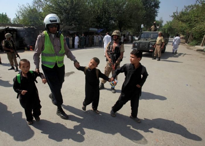 A traffic policeman helps school children cross the road as army soldiers stand guard after suicide bombers attacked a Christian neighborhood in Khyber Agency near Peshawar, Pakistan, September 2, 2016.