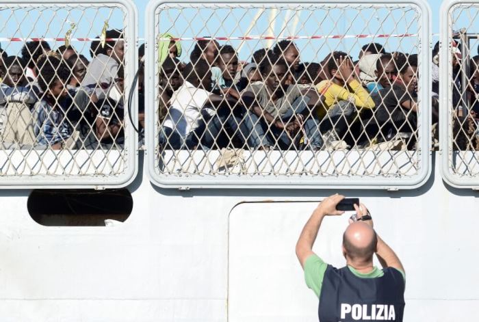 A police officer uses a mobile phone as migrants wait to disembark from the Italian Navy ship Borsini in the Sicilian harbour of Palermo, southern Italy, July 20, 2016.