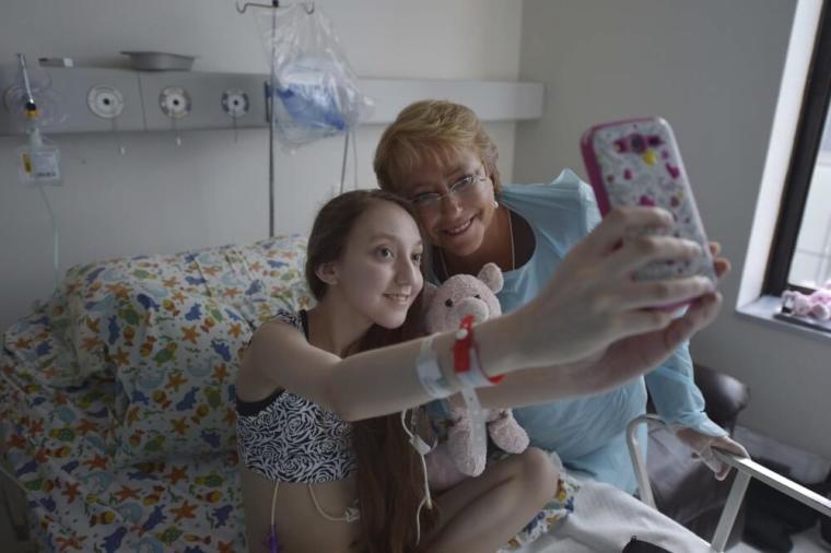 Chile's President Michelle Bachelet (R) poses for a selfie with Valentina Maureira, a 14-year old girl who suffers from cystic fibrosis, at an hospital room in Santiago, February 28, 2015. Maureira made an emotional plea to be allowed to die, filming herself asking Bachelet to authorize her euthanasia. In a video that the media said had been uploaded to her Facebook page on February 22, 2015, Valentina said from her hospital bed: 'I am asking to speak urgently to the president because I am tired of living with this sickness and she can authorize the injection to put me to sleep forever.'