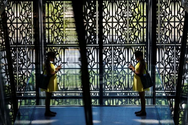 Reflected in glass, a woman stands in front of metal screening panels which make up the “corona” that encloses the National Museum of African American History and Culture on the National Mall in Washington September 14, 2016. The museum will open to the public on September 24.