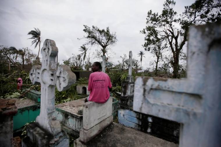 A man sits on a tombstone as he watches other clearing trees after Hurricane Matthew in Les Cayes, Haiti, October 6, 2016.