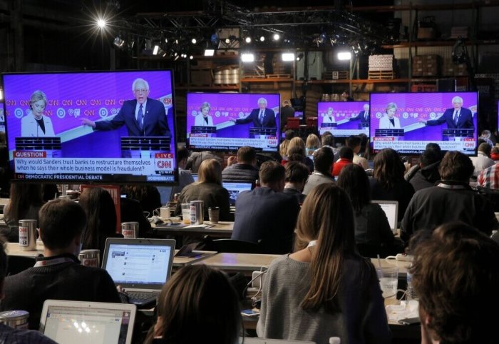 Journalists watch Democratic U.S. presidential candidates Hillary Clinton (L) and Senator Bernie Sanders debate on video screens in the media filing center during a debate hosted by CNN and New York One at the Brooklyn Navy Yard in New York April 14, 2016.
