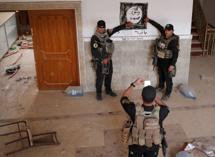 Iraqi special forces soldiers pose for a photograph in front of a Islamic States drawing inside a building located inside a church compound in Bartella, east of Mosul, Iraq October 21, 2016.