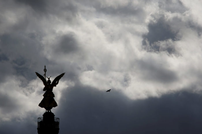A bird flies beside the 'Golden Victoria' monument on top of the Siegessaeule (victory column) as it is silhouetted against a dark cloudy sky in Berlin, Germany, May 15, 2016.