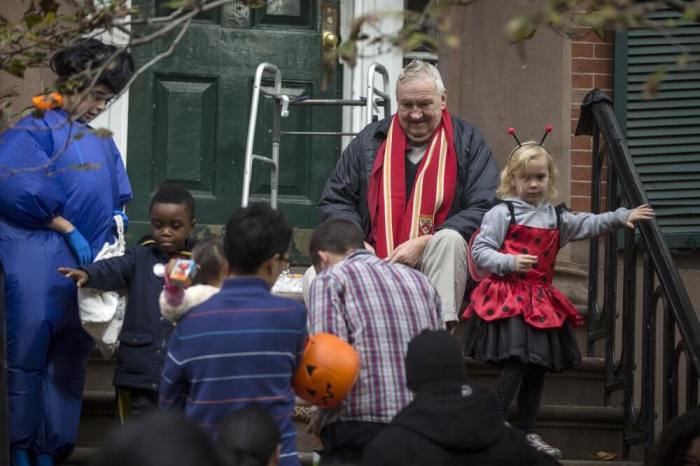 A man sits on his stoop and gives out candy to trick or treaters as they take part in the Children's Halloween day parade at Washington Square Park in the Manhattan borough of New York October 31, 2015.