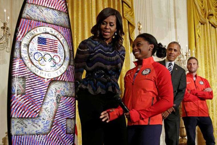 2016 Olympic individual all-around gymnast Simone Arianne Biles presents a surf board to U.S. President Barack Obama and First lady Michelle Obama as he welcomes U.S. Olympic and Paralympics teams at the White House in Washington, September 29, 2016.