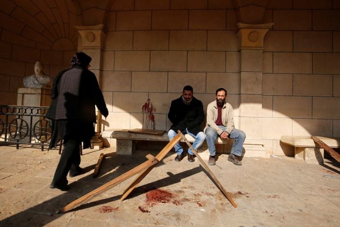 Egyptian Christians sit on a bench near a blood stain on a wall at the scene following a bombing inside Cairo's Coptic cathedral in Egypt December 11, 2016.