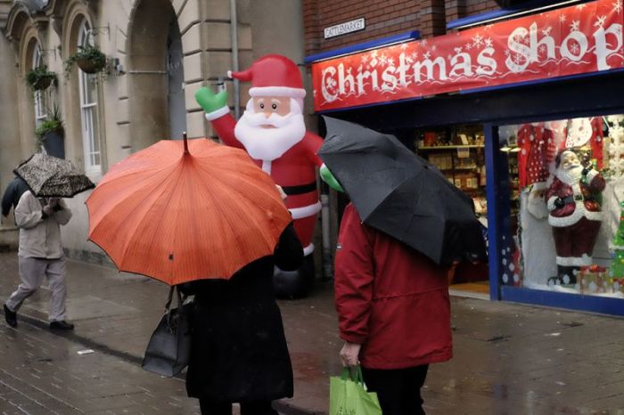 Shoppers walk past a Christmas shop during rainfall in Loughborough, Britain, December 24, 2015.