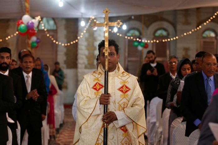 A member of church holds a cross as he walks past people pray during a ceremony on Christmas eve at Central Brooks Memorial Church in Karachi, Pakistan, December 24, 2016.