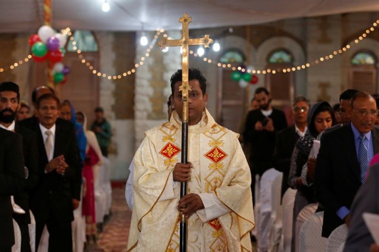 A member of church holds a cross as he walks past people pray during a ceremony on Christmas eve at Central Brooks Memorial Church in Karachi, Pakistan, December 24, 2016.