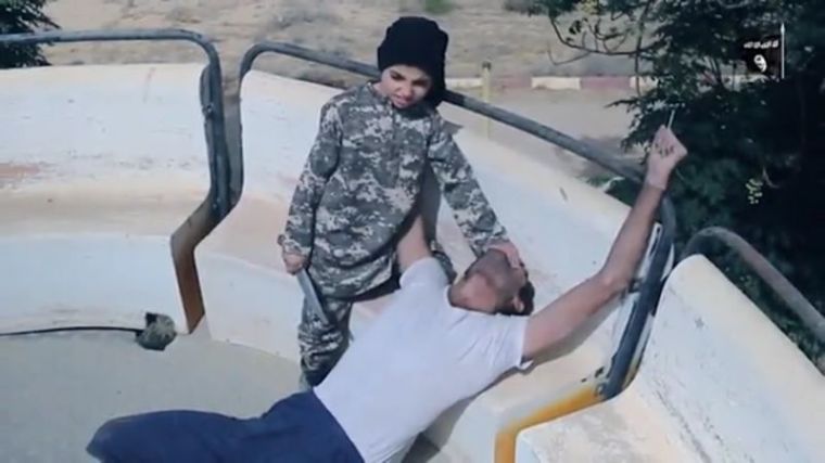 An ISIS child soldier is filmed holding a large knife while he stands over a victim in Syria in a video released in January 2017.