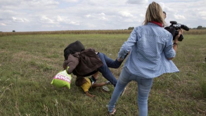 A migrant carrying a child falls after tripping on TV camerawoman (R) Petra Laszlo while trying to escape from a collection point in Roszke village, Hungary, September 8, 2015.