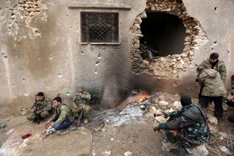 Rebel fighters rest near a hole in the wall by a fire on the outskirts of the northern Syrian town of al-Bab, Syria, January 15, 2017.