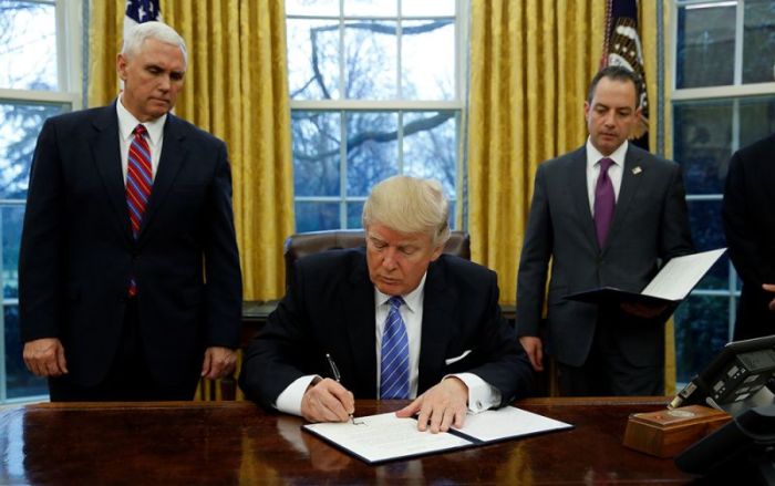 U.S. President Donald Trump signs an executive order on U.S. withdrawal from the Trans Pacific Partnership while flanked by Vice President Mike Pence (L) and White House Chief of Staff Reince Priebus (R) in the Oval Office of the White House in Washington January 23, 2017.