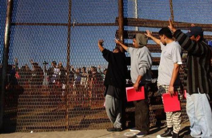 A group of recently deported immigrants stand near the double steel fence that separates San Diego and Tijuana at the border in Tijuana December 10, 2011.