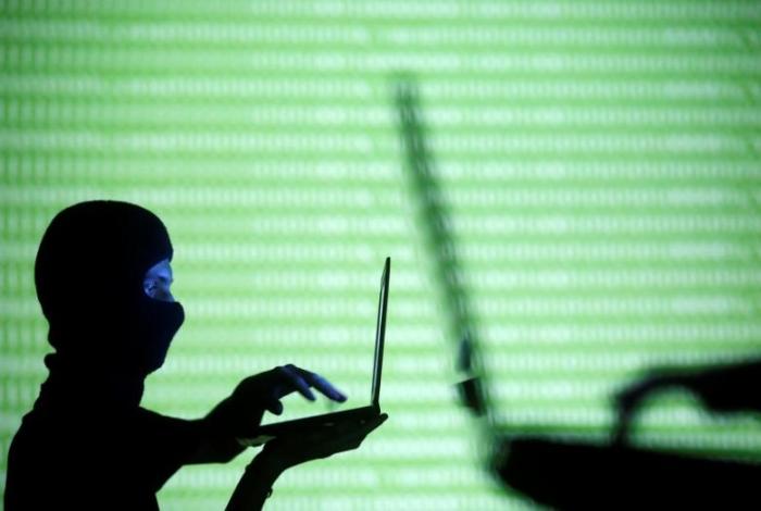 File: People wearing balaclavas are silhouetted as they pose with a laptops in front of a screen projected with the word 'cyber' and binary code, in this picture illustration taken in Zenica October 29, 2014.