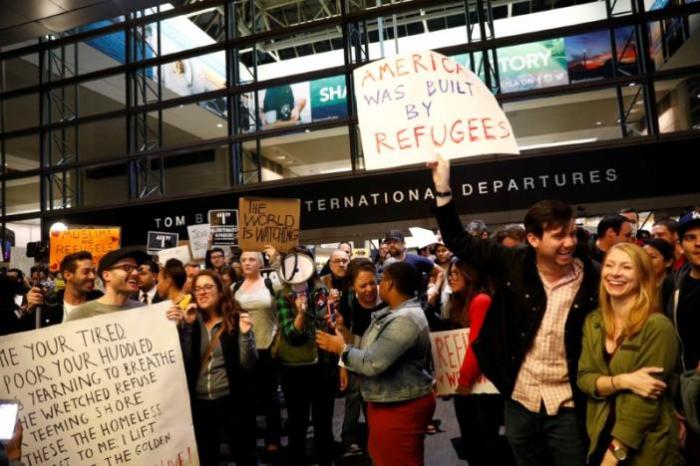 Protesters hold signs in opposition to U.S. President Donald Trump's ban on immigration and travel outside Terminal 4 at JFK airport in Queens, New York City, New York, U.S. January 29, 2017.