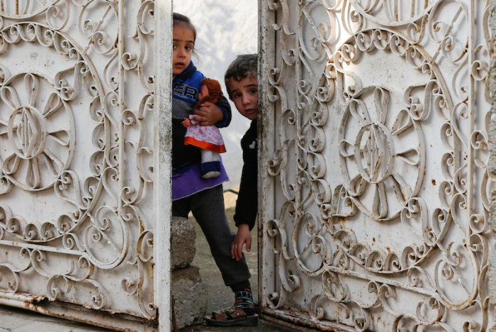 Iraqi children stand behind the doors of their home during a fight with Islamic State militants in Rashidiya, North of Mosul, Iraq, January 30,2017.