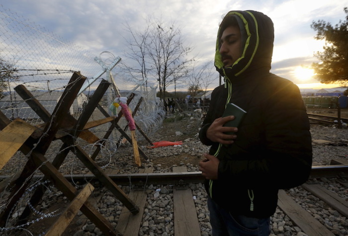 A stranded Iranian Christian migrant holds the Bible as he prays at dawn in front of a fence reinforced by barbed wire and a wooden barricade at the Greek-Macedonian border near to the Greek village of Idomeni November 30, 2015.