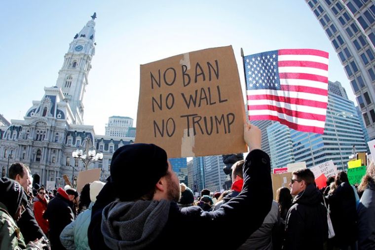 Protester Brandon McTear holds a sign and the American Flag as demonstrators gather to protest against U.S. President Donald Trump's executive order placing a temporary pause on refugee resettlement from seven primarily Muslim countries from entering the United States during a rally in Philadelphia, Pennsylvania, February 4, 2017